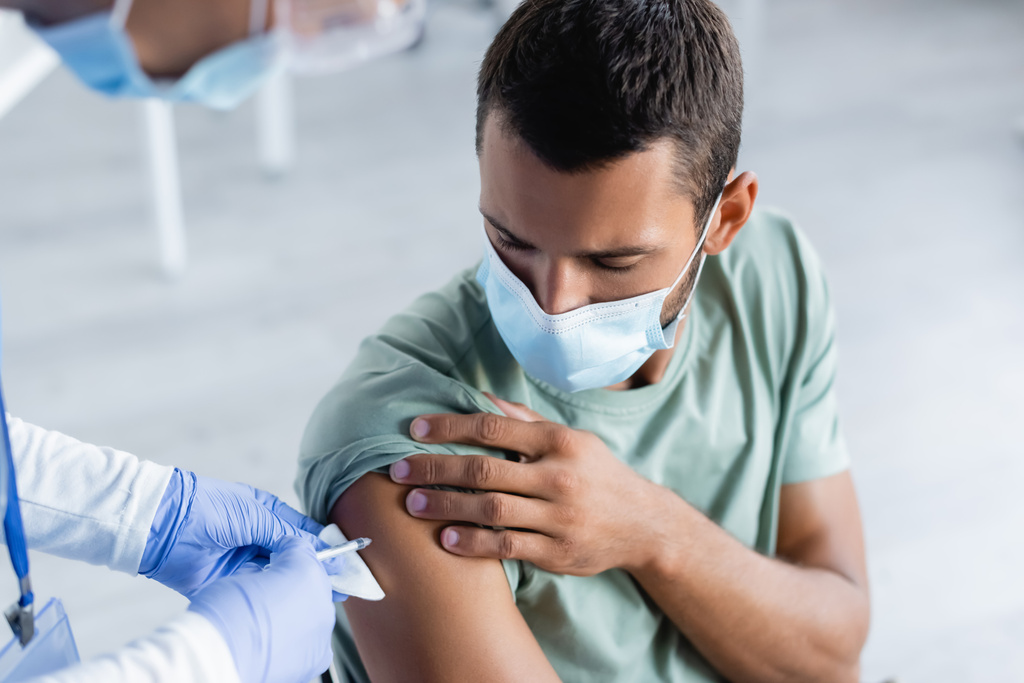 保護マスクの青年にワクチンを注射するぼやけた看護師 - 写真・画像