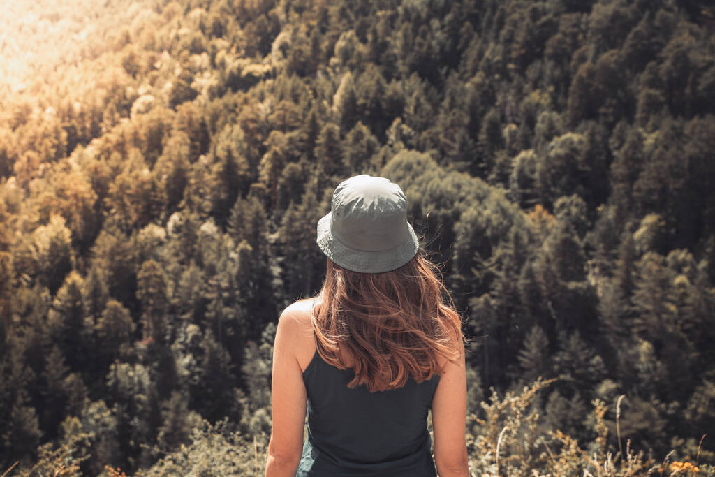 Fiatal nő áll egyedül a szabadban vad erdők hegyek a háttérben. Utazó életmód és túlélés koncepció hátsó nézet. Trekking zöld kalapban. - Fotó, kép