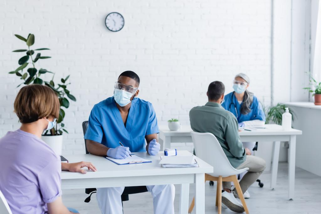 Interrasszista orvosok orvosi maszkban, akik az oltási központban dolgoznak betegekkel. - Fotó, kép