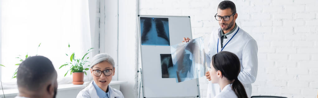 молодий лікар, який демонструє рентгенівські промені для багатоетнічних колег, банер
 - Фото, зображення