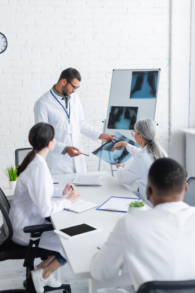 érett orvos rámutatva tüdő röntgen a tanács alatt többnemzetiségű kollégák - Fotó, kép