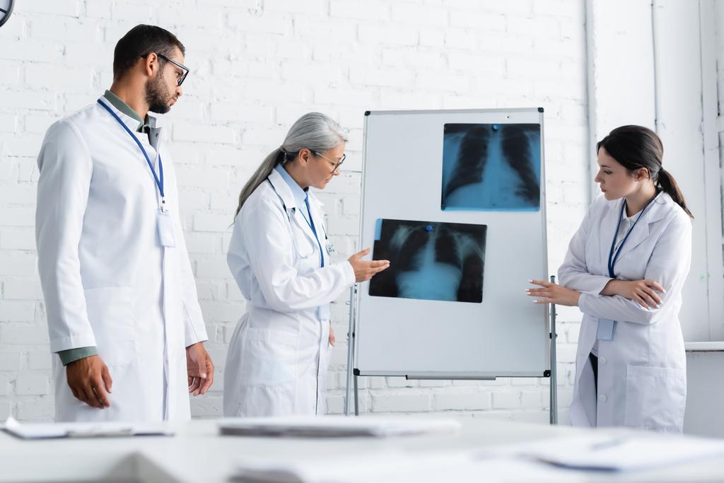 mature asiatique médecin pointant poumons X-ray sur flip chart près de jeunes collègues - Photo, image