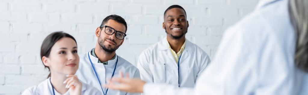 multiethnic doctors smiling near mature colleague talking on blurred foreground, banner - Photo, Image