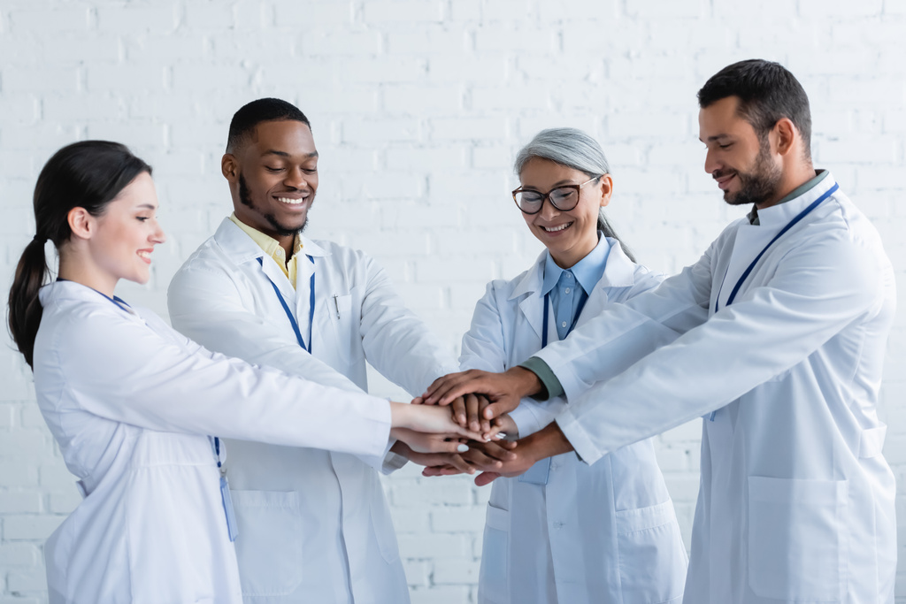 médecins multiethniques joyeux debout avec les mains jointes dans la clinique - Photo, image