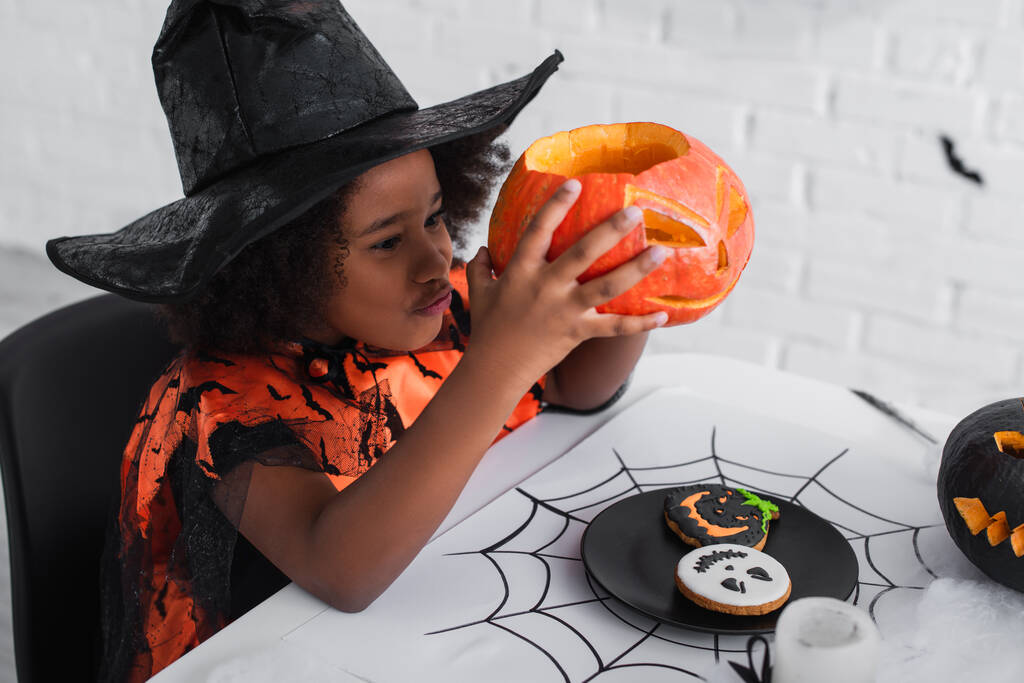 happy african american girl in witch halloween costume holding caved pumpkin - Photo, Image