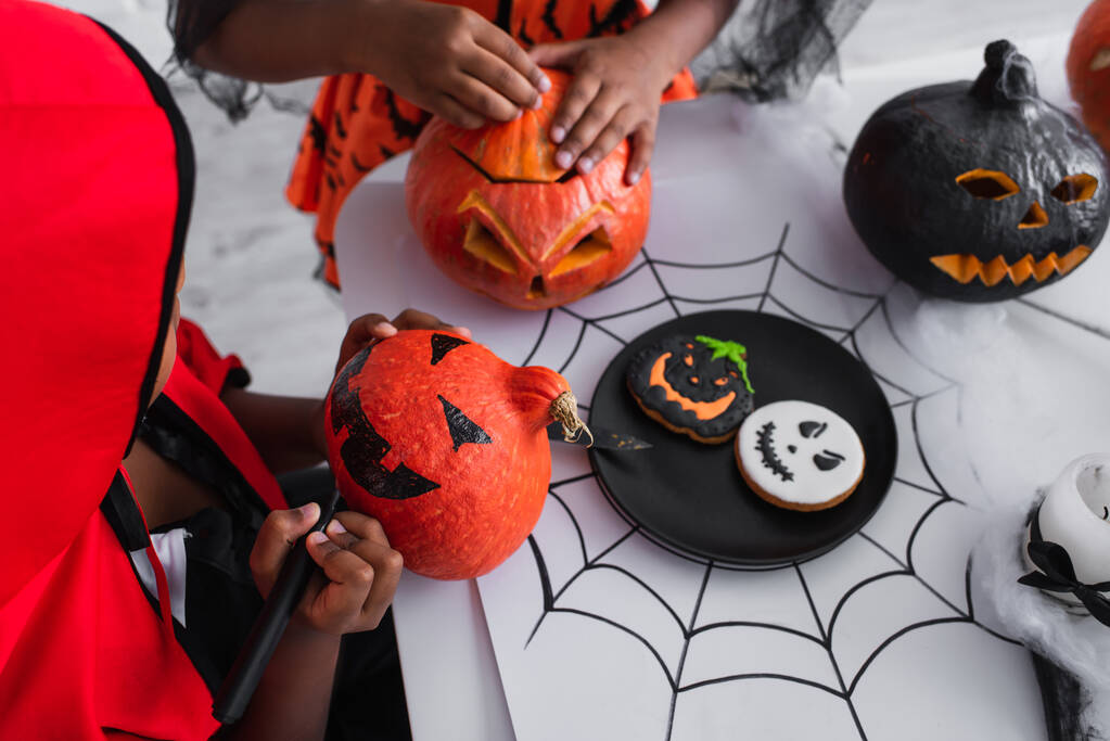 africano americano niño en halloween traje dibujo en calabaza cerca hermana - Foto, imagen