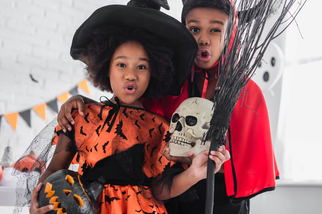 niños afroamericanos espeluznantes con disfraces de Halloween sosteniendo el cráneo, calabaza tallada y escoba  - Foto, imagen