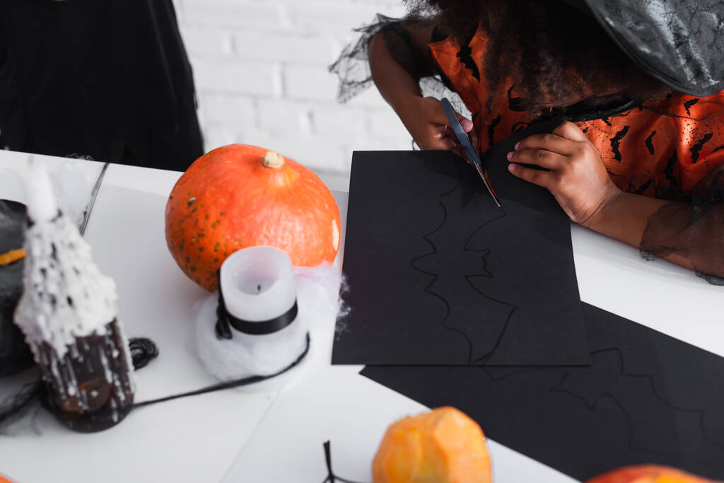 vista recortada del niño afroamericano cortando cartón negro con plantilla de murciélago - Foto, Imagen