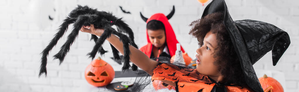 africký americký dívka v čarodějnice kostým držení hračka pavouk v blízkosti rozmazaný bratr, prapor - Fotografie, Obrázek
