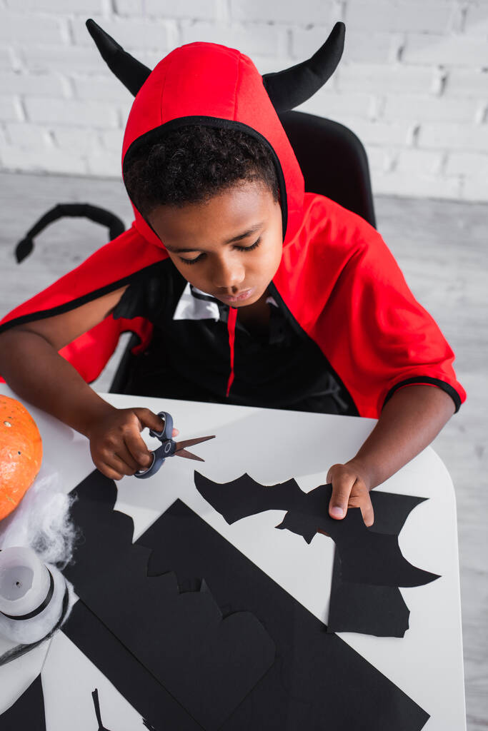 vista ad alto angolo di ragazzo africano americano in costume di Halloween con forbici e pipistrello taglio carta  - Foto, immagini