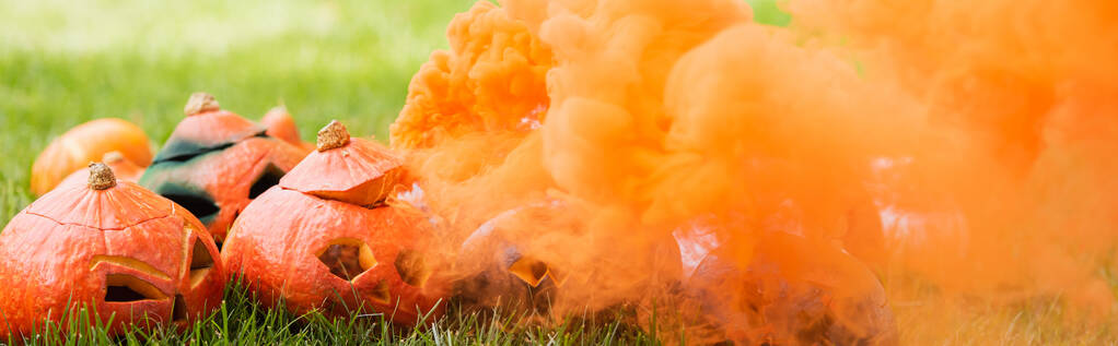 fumée orange près de citrouilles sculptées sur pelouse verte, bannière - Photo, image