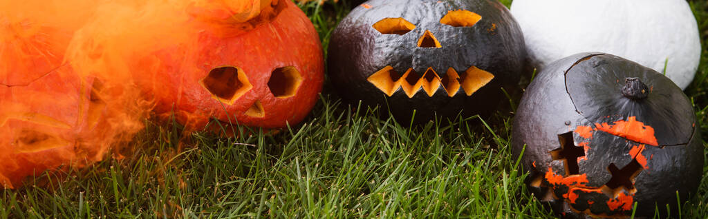 orange smoke near carved and spooky pumpkins on green lawn, banner - Photo, Image