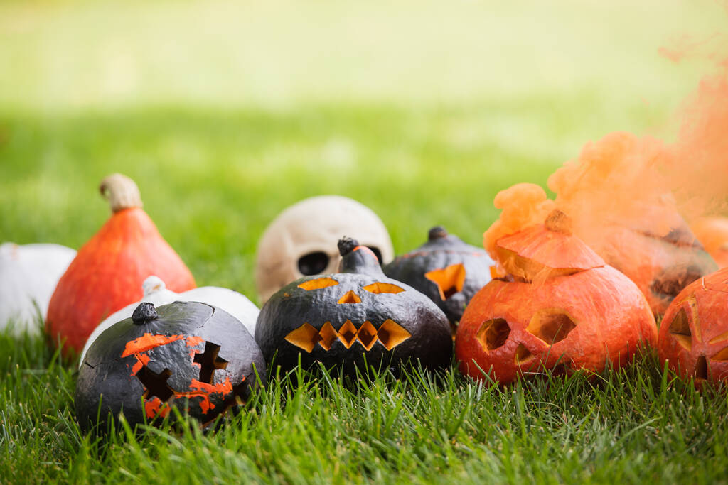 abóboras esculpidas e assustadoras com fumaça de laranja perto do crânio borrado no gramado verde - Foto, Imagem