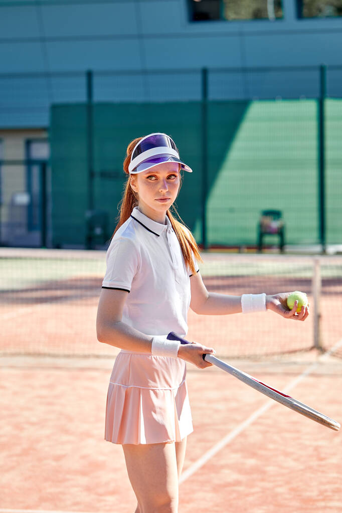 Приваблива молода руда жінка, що стоїть на тенісному корті, тримає тенісну ракетку
 - Фото, зображення