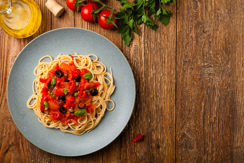 Italienische Spaghetti alla Pultanesca mit Tomaten und Oliven. Serviert ohne Fleisch und Käse. Ansicht von oben. Natürlicher hölzerner Hintergrund.  - Foto, Bild