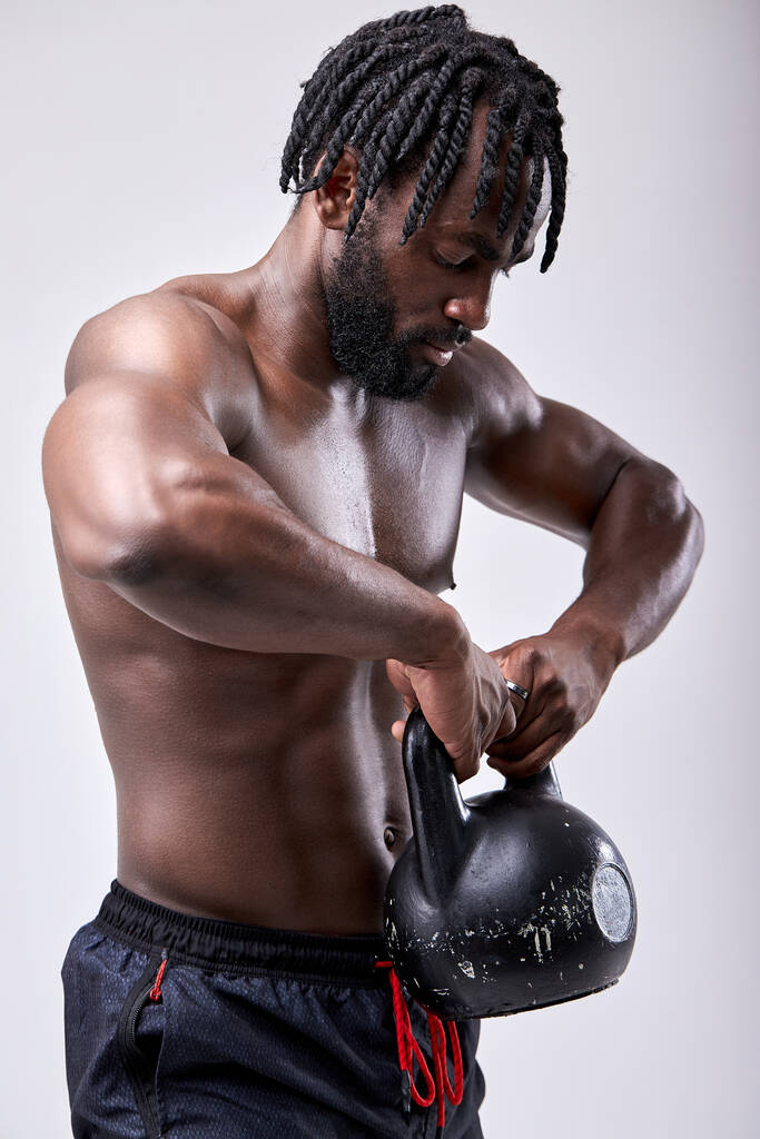 Athletischer junger afrikanischer Mann, der mit einer Wasserkocher-Glocke trainiert. Isolierter weißer Hintergrund - Foto, Bild