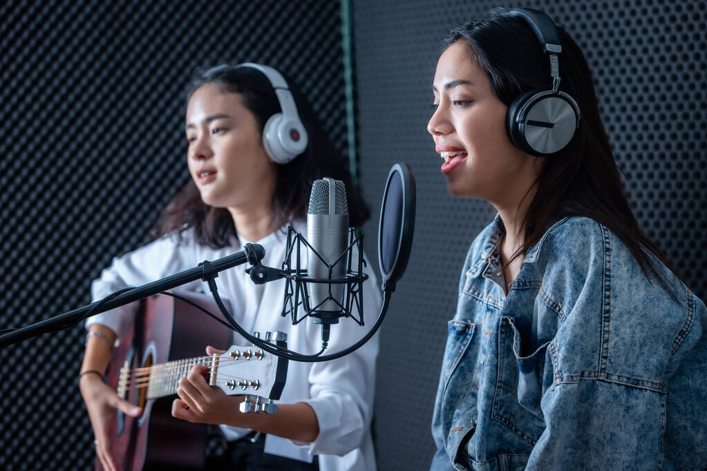 Joyeux sourire joyeux de portrait Deux jeunes chanteuses asiatiques portant un casque avec une guitare enregistrant une chanson devant le microphone dans un studio professionnel - Photo, image