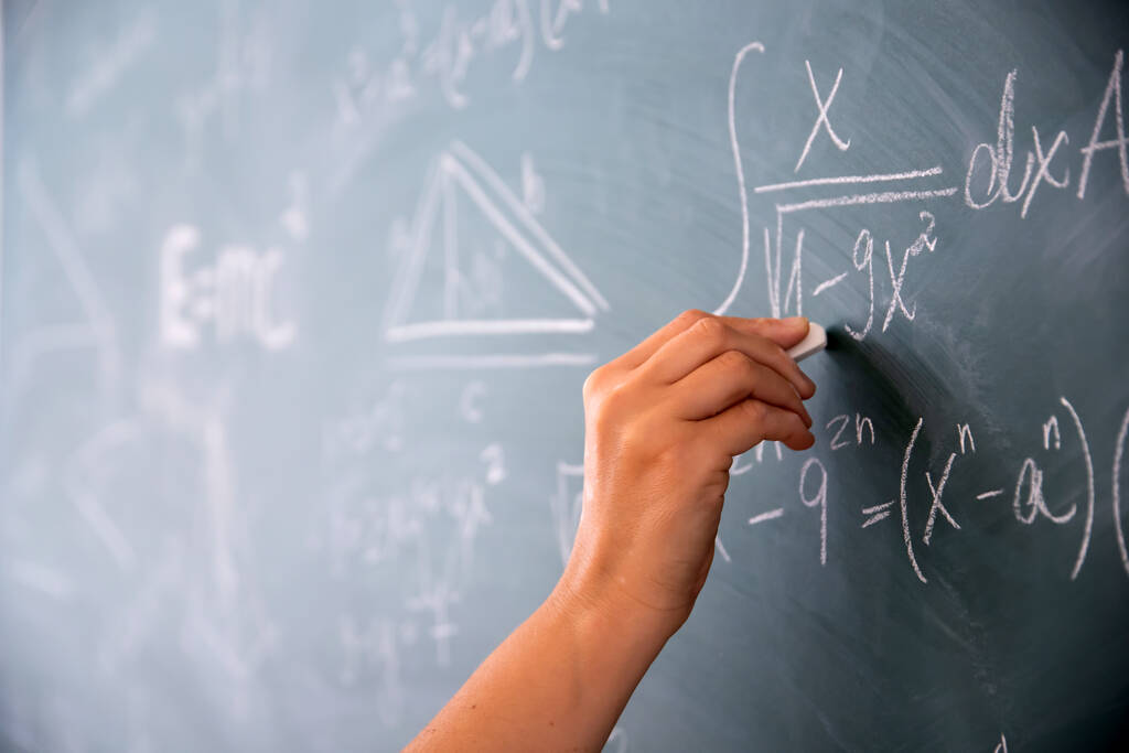 Een close-up van een hand met krijt en wiskundige vergelijkingen op het schoolbord. Onderwijsconcept. - Foto, afbeelding