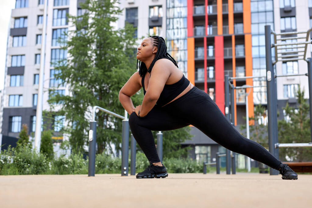obesa grasa africana mujer haciendo ejercicios de estiramiento en el campo de deportes antes de entrenar - Foto, imagen