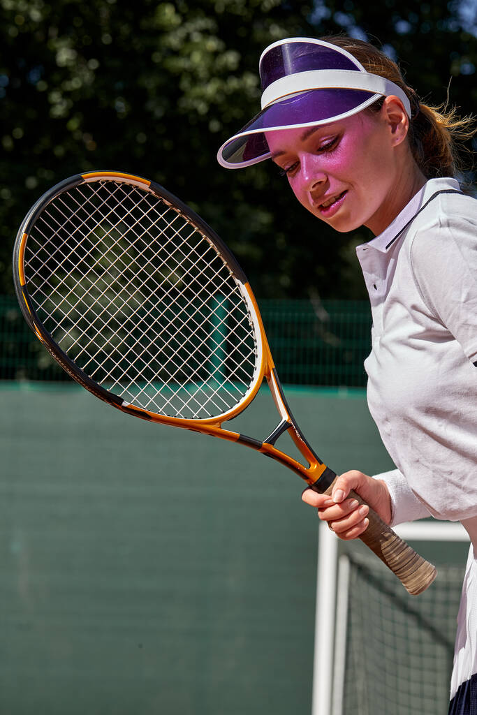 Csinos fiatal nő fehér egyenruhában tartja Tenisz ütő a kezében - Fotó, kép