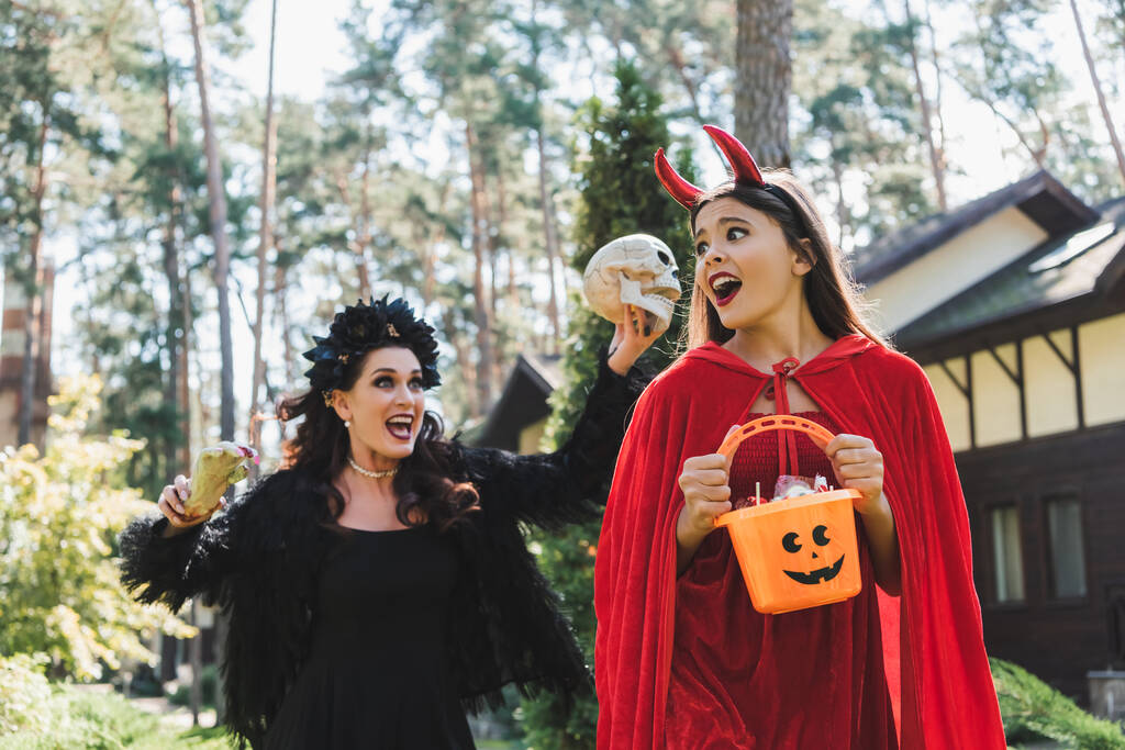 mujer en vampiro halloween traje gritando y asustando hija con cráneo y juguete mano - Foto, imagen