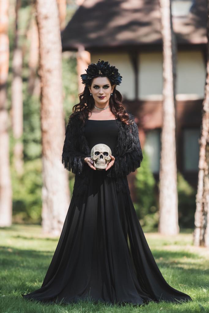 Frau im schwarzen Halloween-Kostüm mit gruseligem Totenkopf im Freien - Foto, Bild