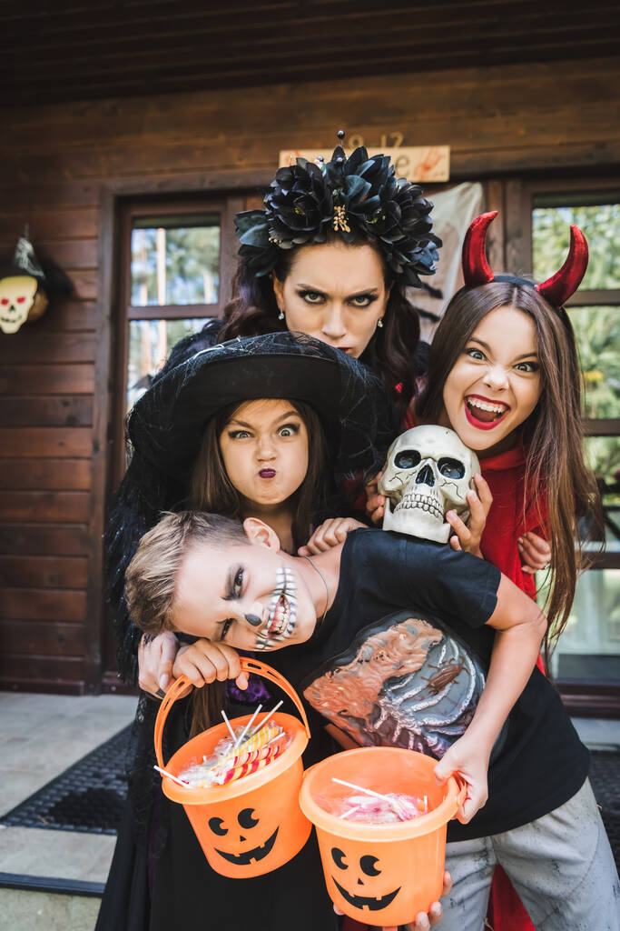 famiglia in costumi di Halloween, con teschio spettrale e secchio di caramelle smorfie e ringhiare alla macchina fotografica - Foto, immagini