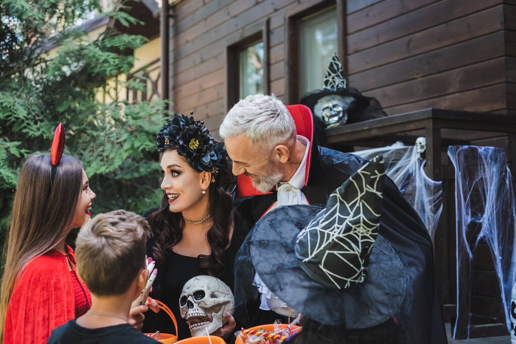 familia feliz en trajes espeluznantes de Halloween sonriendo cerca de la casa de madera - Foto, imagen