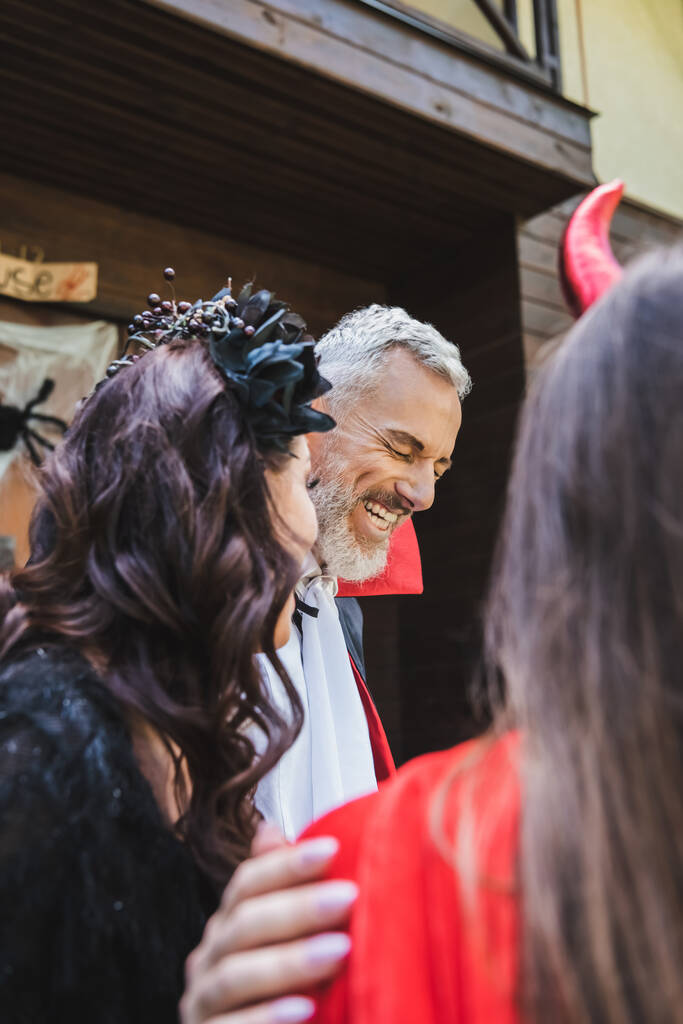 vzrušený muž smích se zavřenýma očima v blízkosti rozmazané manželky a dcery na Halloween - Fotografie, Obrázek