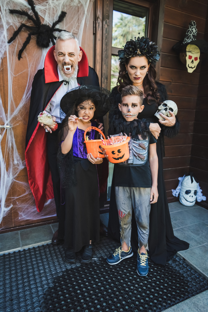 familia espeluznante en trajes de Halloween de muecas en el porche con decoración - Foto, imagen