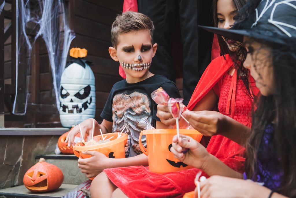 lapset pelottava halloween puvut istuu kuistilla ämpäreittäin makeisia - Valokuva, kuva