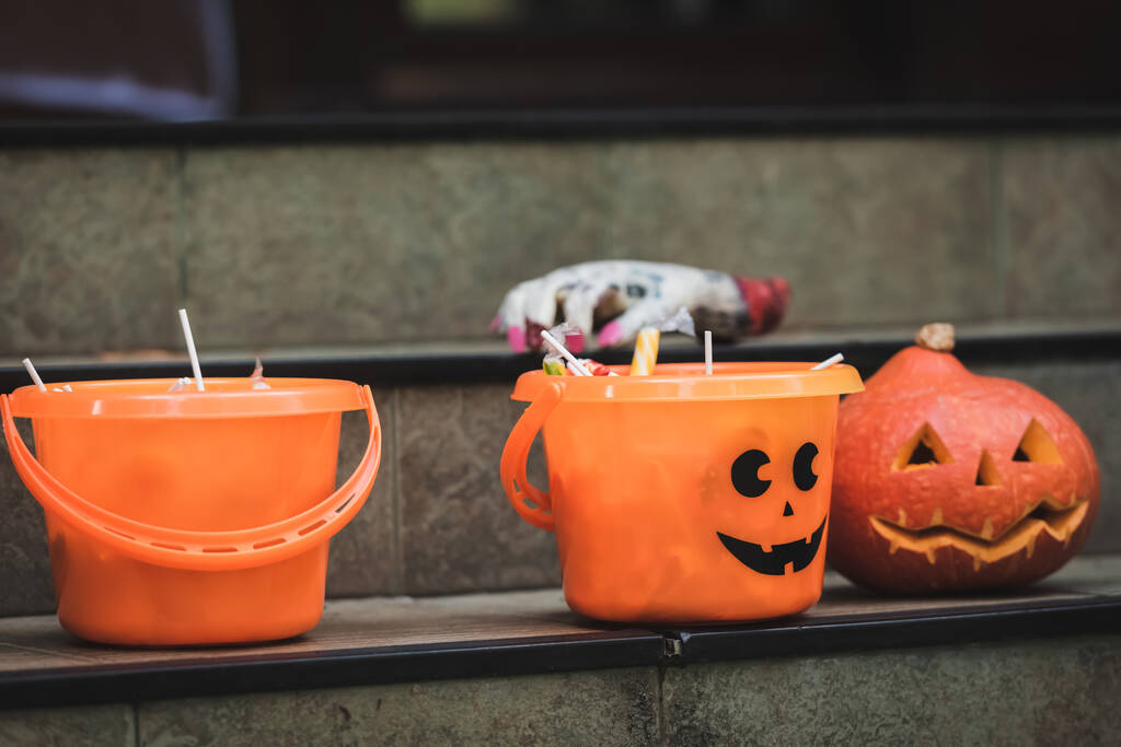 halloween emmers met snoep in de buurt van gesneden pompoen en wazig speelgoed hand op de trap - Foto, afbeelding