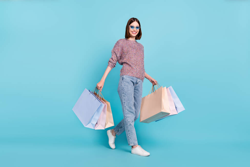 Photo of traveler lady walk carry store bags wear sunglass sweater jeans shoes isolated blue color background - Photo, Image