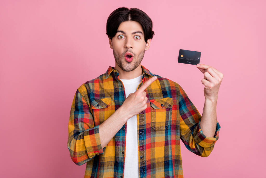Fotografie ohromen legrační mladý muž oblečený kostkované oblečení ukazující prstem kreditní karty izolované růžové barvy pozadí - Fotografie, Obrázek
