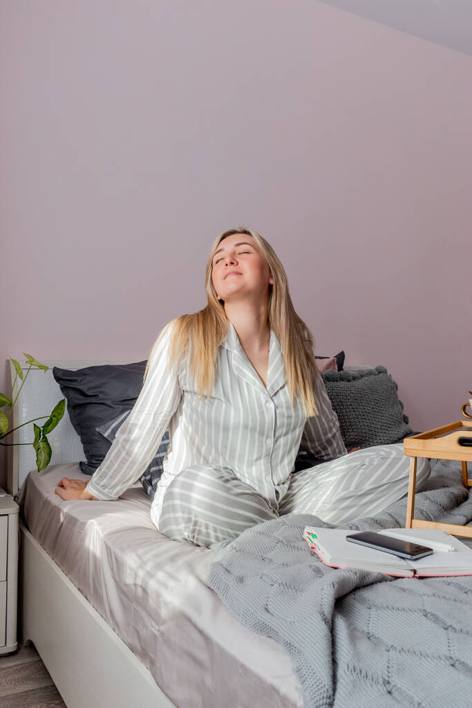 Young business woman meditates while sitting on the bed, after work Internet using a computer. Girl listens calm music near the laptop. Home comfort zone and wellness concept. - Photo, Image