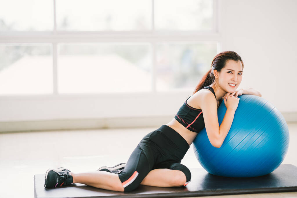 Happy young Asian woman health exercise alone at home gym or sports club, rest on fitness ball. Yoga aerobic class, sport trainer, weight loss, or healthy wellbeing lifestyle concept. With copy space - Photo, Image