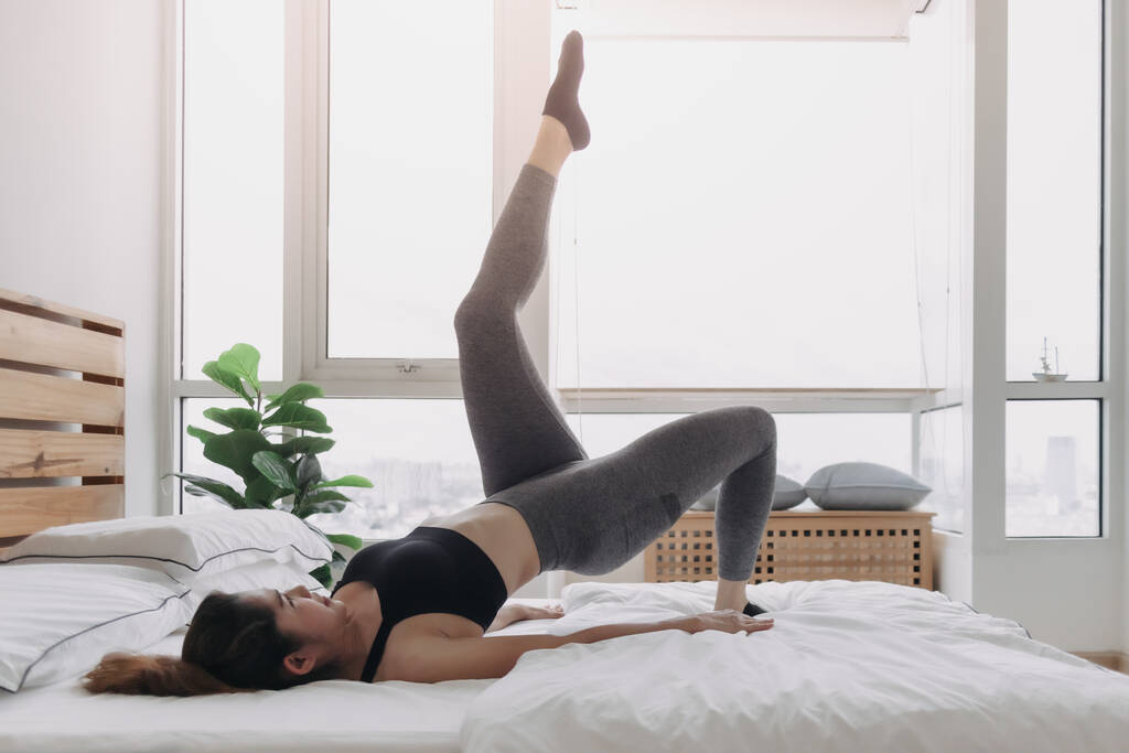 Γυναίκα κάνει Εναλλασσόμενο Πόδι Αύξηση προπόνηση στο διαμέρισμά της κρεβατοκάμαρας. - Φωτογραφία, εικόνα