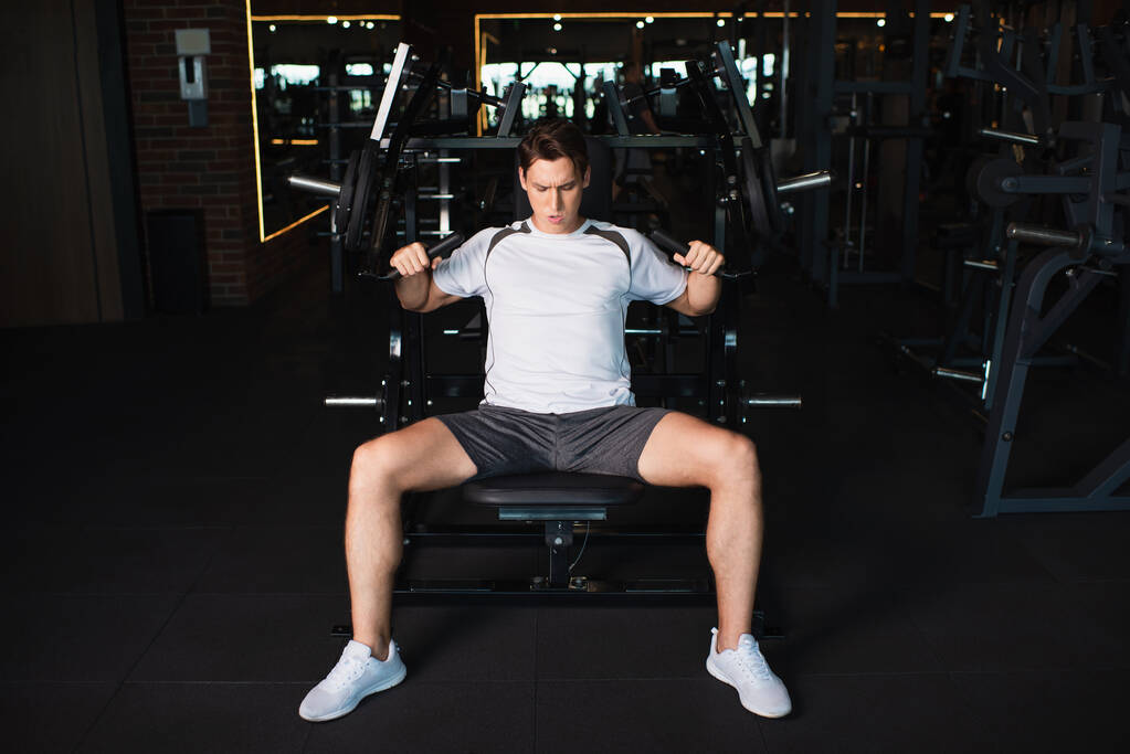 vue pleine longueur de l'homme athlétique travaillant sur l'extension du bras machine d'exercice dans la salle de gym - Photo, image