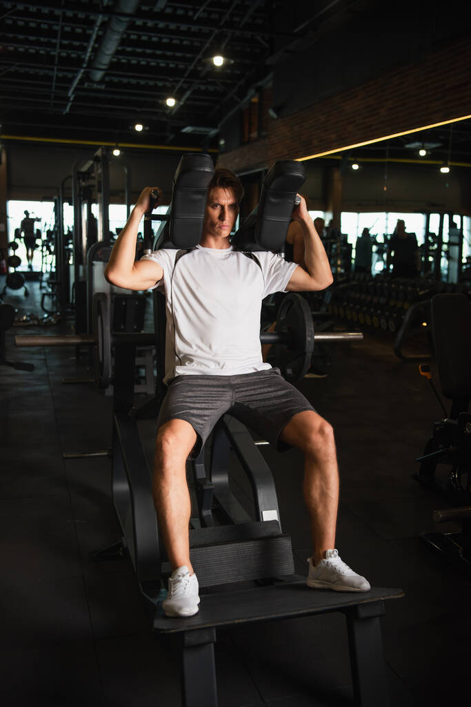 体育館での腕拡張運動マシンに関するスポーツマンのトレーニングの完全な長さのビュー - 写真・画像