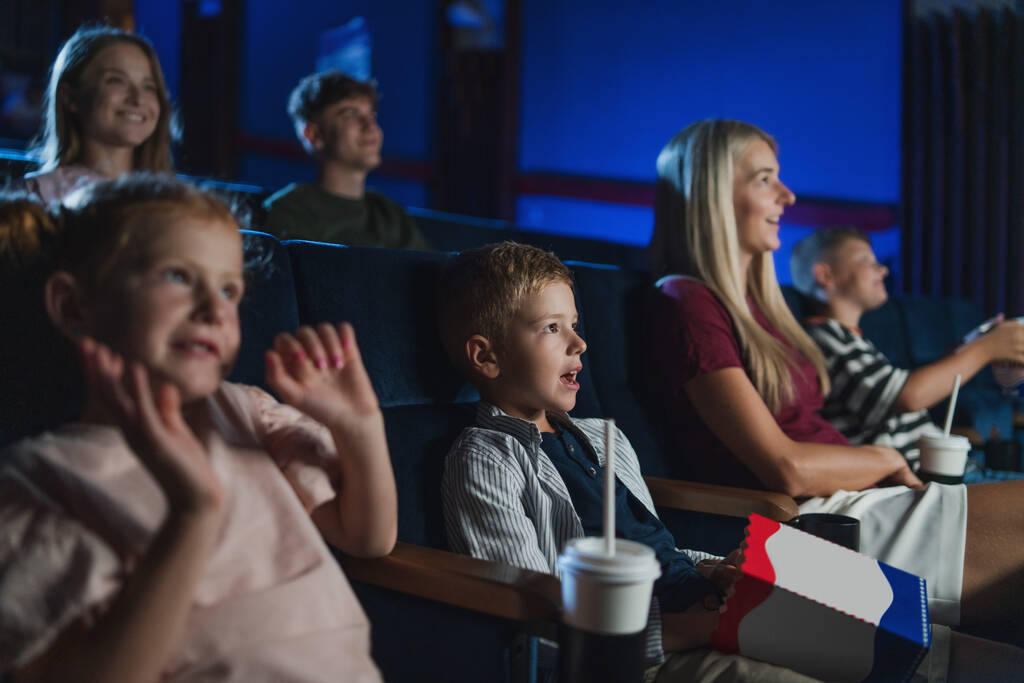 Matka ze szczęśliwymi małymi dziećmi w kinie, ogląda film. - Zdjęcie, obraz