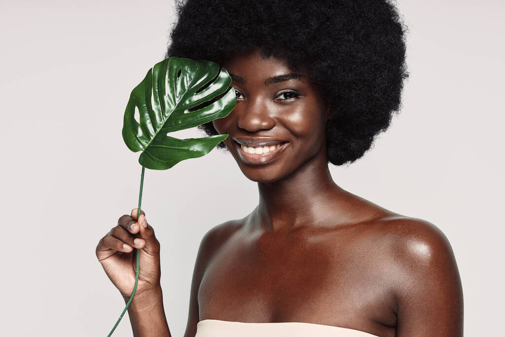 Muotokuva kaunis nuori afrikkalainen nainen tilalla kasvi lähellä kasvoja ja hymyillen - Valokuva, kuva