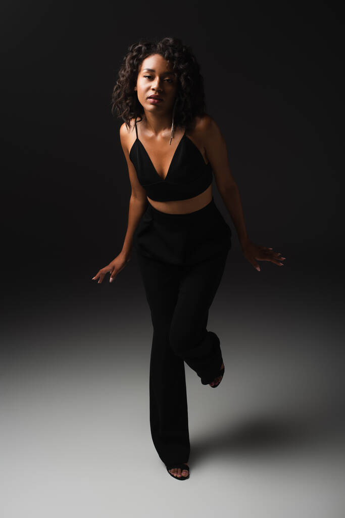 in voller Länge sexy afrikanisch-amerikanische Frau in stilvollem Outfit posiert auf schwarz  - Foto, Bild