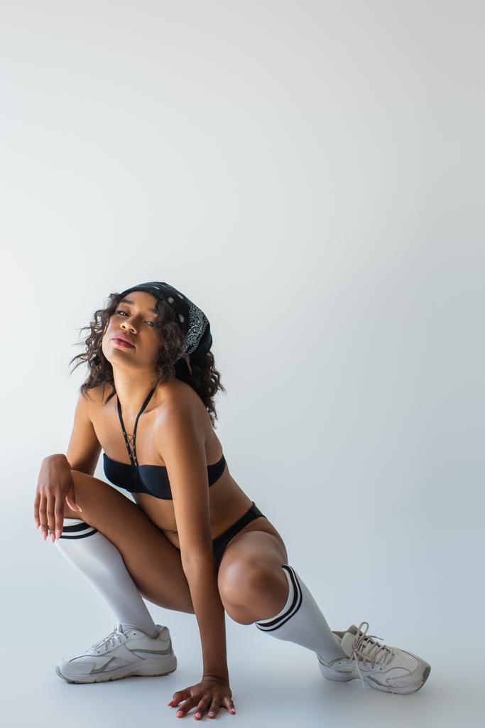 sexy afrikanisch-amerikanisches Model in Badeanzug, kniehohen Socken und Turnschuhen posiert auf grau - Foto, Bild