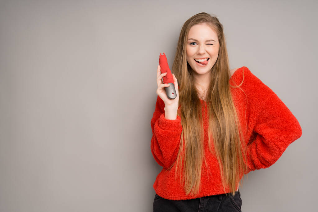 A pretty white-skinned girl happily holds a red rubber penis in her hands.Useful for a sex shop - Zdjęcie, obraz