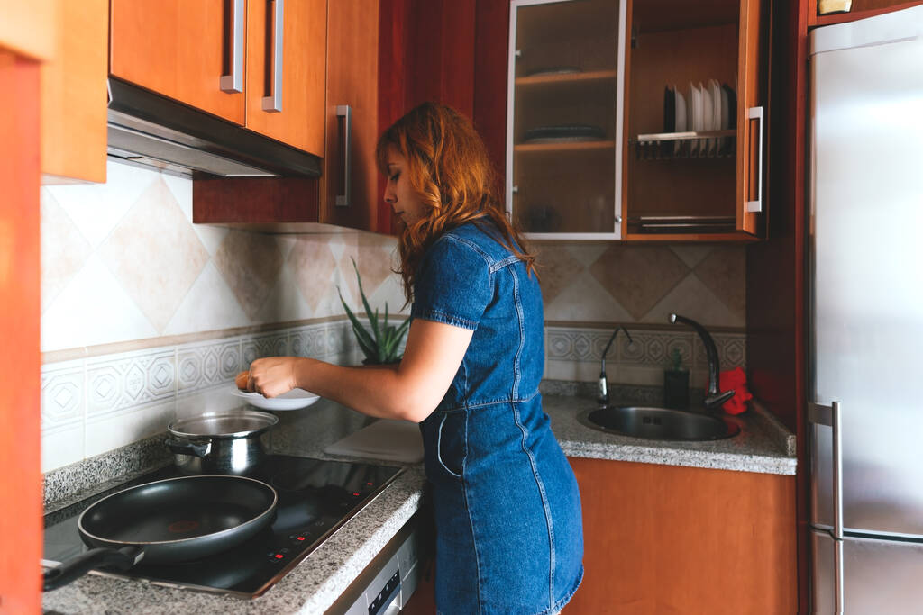 Una joven ama de casa caucásica sacando los huevos cocidos de una olla de acero inoxidable en la cocina - Foto, imagen