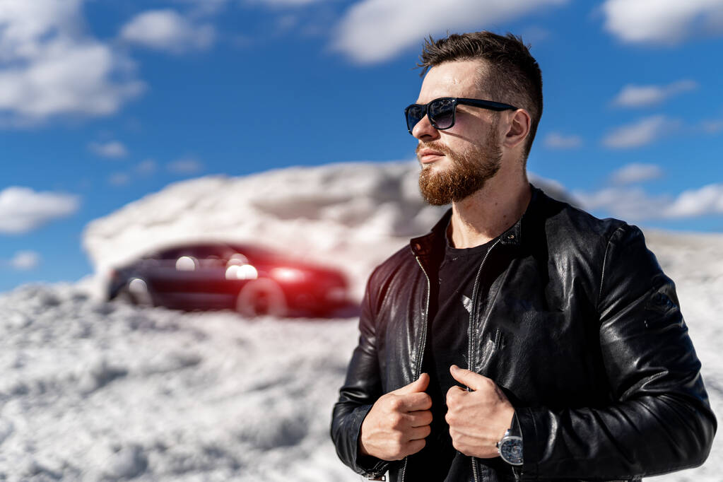 Schöner Mann mit Sonnenbrille, der mit seinem Auto im Hintergrund auf der Straße steht. Verkehrskonzept. Horizontales Foto - Foto, Bild
