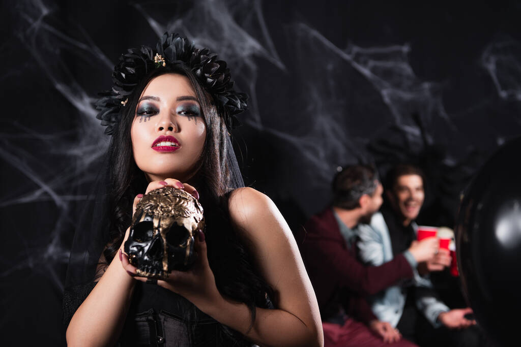 asiatische Frau im Vampir-Halloween-Kostüm zeigt gruseligen Totenkopf vor der Kamera auf schwarz - Foto, Bild