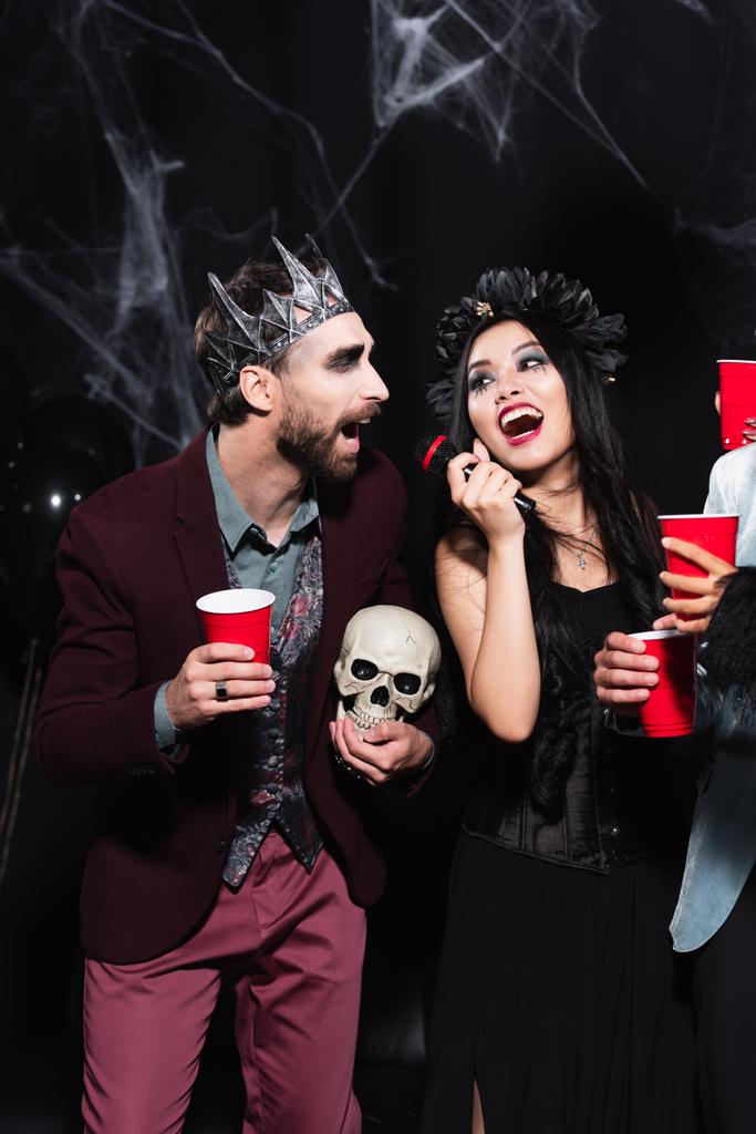 asiatico donna in vampiro halloween costume canto karaoke con uomo in corona su nero - Foto, immagini