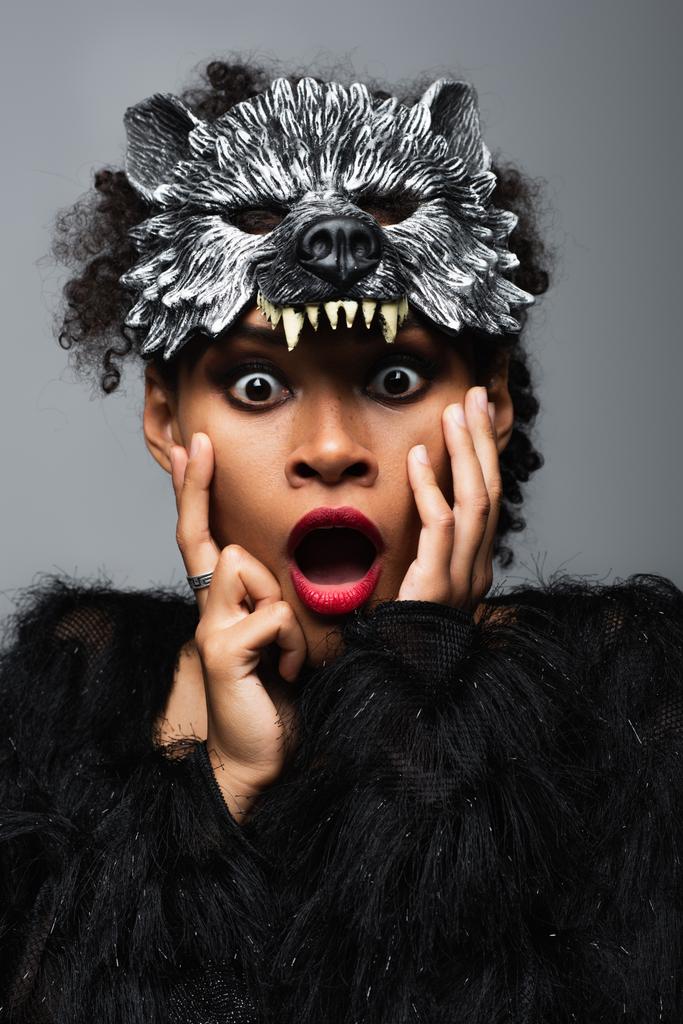 järkyttynyt afrikkalainen amerikkalainen nainen ihmissusi halloween naamio koskettaa kasvot eristetty harmaa - Valokuva, kuva