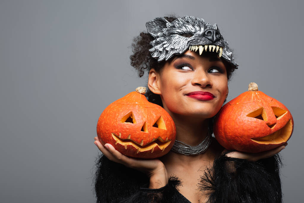 potěšen africký Američan žena v vlkodlak halloween maska držení vyřezávané dýně izolované na šedé - Fotografie, Obrázek